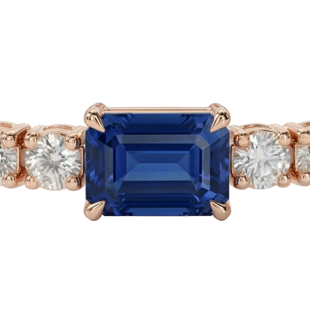 alt="close up view of lab grown emerald cut blue sapphire and round diamond east-west tennis bracelet in 14k rose gold"