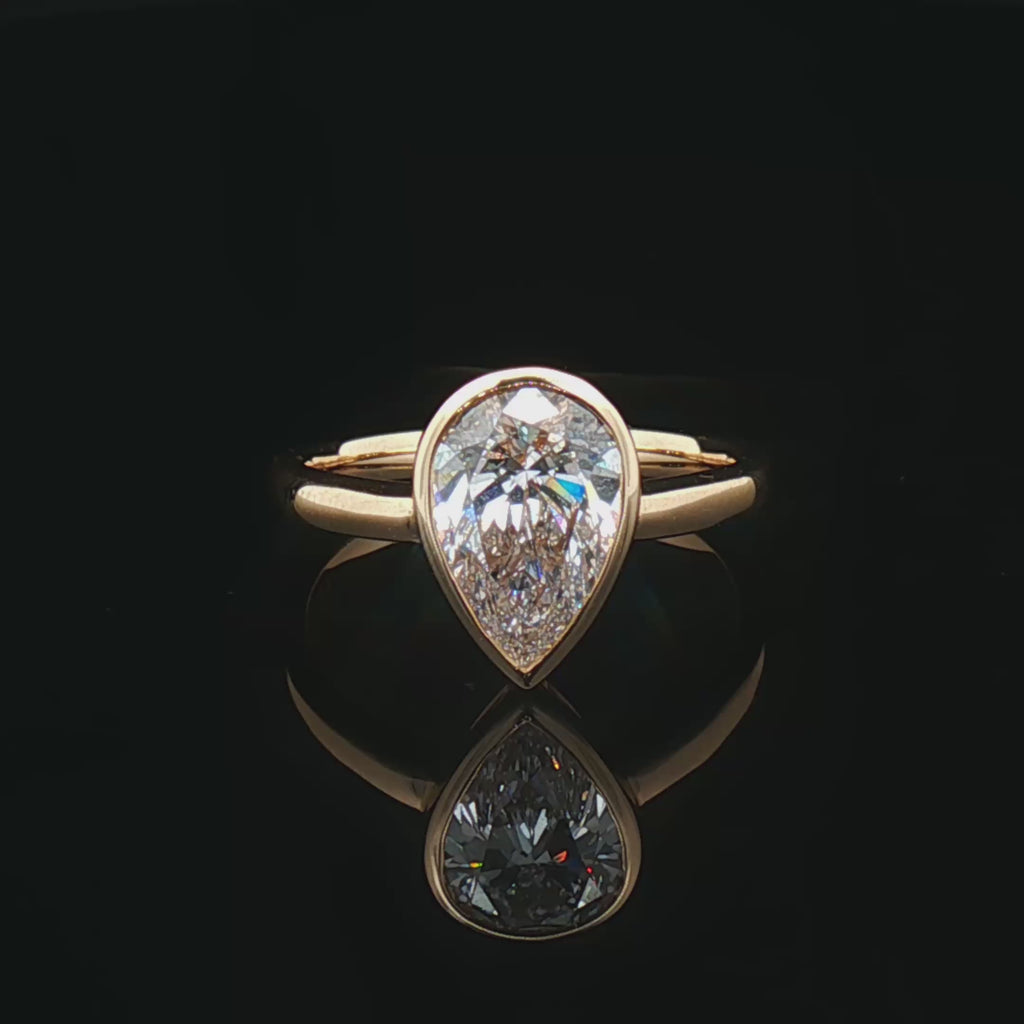 alt="360 video of lab grown pear cut diamond bezel set engagement ring in 14K yellow gold"
